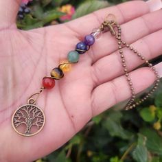 a hand holding a tree of life charm with seven chakras on it's chain