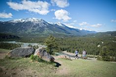 two people are walking up a hill with mountains in the background and trees on either side