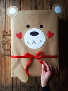 a person holding a brown paper bag with a teddy bear on it and a red ribbon