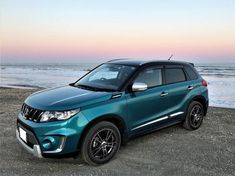 a blue suv parked on the beach at sunset