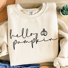 a white sweatshirt with the words hello pumpkin printed on it next to some shoes and a plant