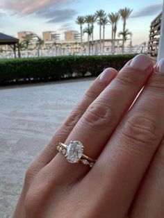 a woman's hand holding an engagement ring with a diamond in the middle and palm trees in the background