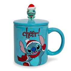 a blue coffee mug with a cartoon character on the lid and an image of a santa hat