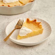 a slice of lemon pie on a plate with a fork next to the pie dish