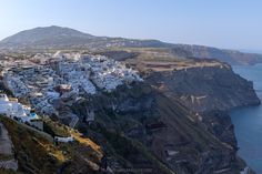 an aerial view of a village on the edge of a cliff by the ocean with mountains in the background