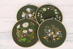 four embroidered hoops with flowers on them sitting on a white wooden surface, one is green and the other is yellow