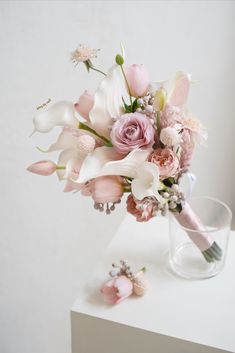 a bouquet of flowers sitting on top of a white table next to a glass vase