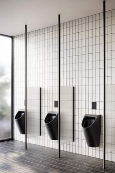 three black urinals in a public restroom with tiled walls and flooring,