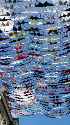 many different colored objects are hanging from the ceiling in front of a building with a blue sky