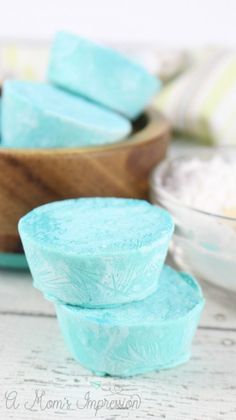 three blue soaps sitting next to each other on a white wooden table with bowls in the background