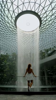 a woman in a white dress is walking under a fountain