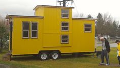 a yellow tiny house sitting on top of a lush green field