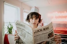 a woman reading a news paper with a chef's hat on top of her head