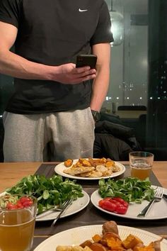 a man standing in front of a table filled with plates of food and drinks, looking at his cell phone