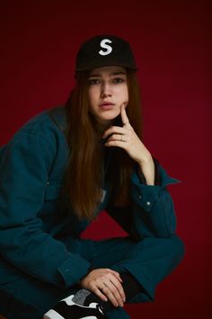 a woman sitting on top of a wooden table wearing a baseball cap and holding her hand to her chin