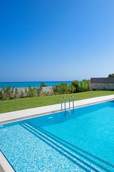 an empty swimming pool in front of the ocean on a sunny day with clear blue skies