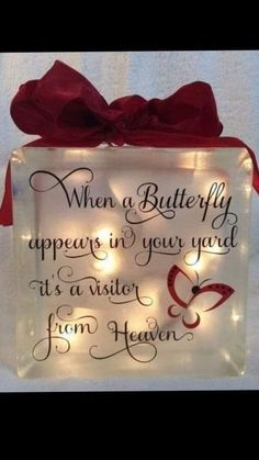 a lighted glass block with a red bow on it's side that says, when a butterfly appears in your yard, it is a visitor from heaven