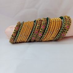 a stack of gold colored bangies with green and pink stones on each one side