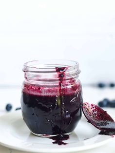 a glass jar filled with blueberry jam on top of a white plate next to a spoon