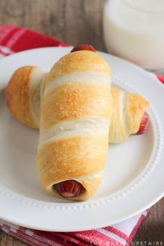 two hotdogs wrapped in bread on a plate next to a glass of milk