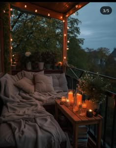 a porch covered in candles and blankets with flowers on the side table next to it