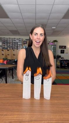 a woman standing behind two paper bags with faces drawn on them and flames in the air