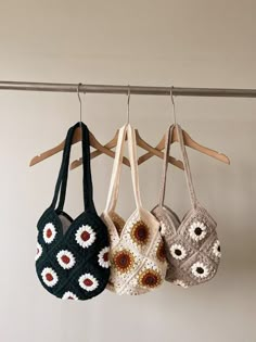 three crocheted purses hanging on a wooden rack in front of a white wall