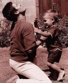 an old black and white photo of a young man playing with a small child in the yard