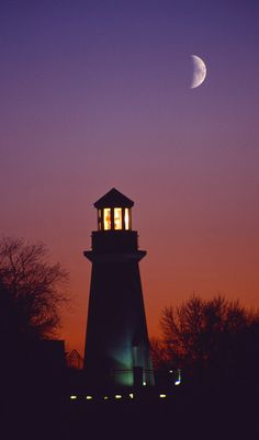 the moon is setting behind a light house