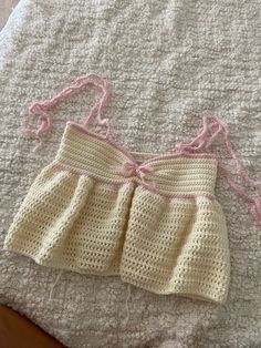 a crocheted baby's dress is laying on a white blanket with pink trim