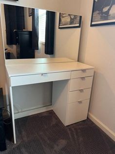 a white desk with two drawers and a mirror on the wall next to it in a room