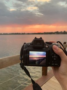 a person is holding up a camera to take a photo on the pier at sunset