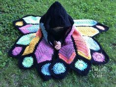 a crocheted butterfly blanket on the ground with someone covering it's face