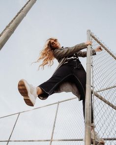 a woman standing on top of a metal fence next to a tall pole with her hair blowing in the wind