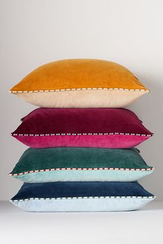 four pillows stacked on top of each other in different colors and sizes, all lined up against a white wall