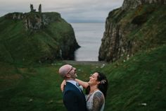 a man and woman standing next to each other on top of a lush green hillside