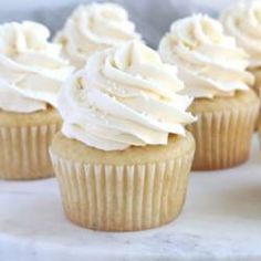 four cupcakes with white frosting sitting on a table