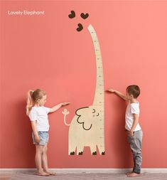 two children are measuring the height of a giraffe wall decal with hearts