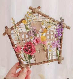 a hand holding up a house made out of paper with flowers on the front and side