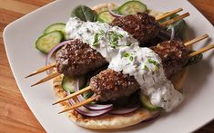 a plate topped with meatballs and veggies on skewered sticks next to cucumbers