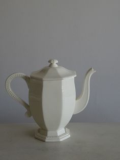 a white tea pot sitting on top of a table next to a gray wall and floor