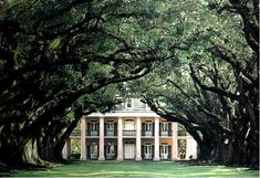 a large white house surrounded by trees in the middle of a field with green grass