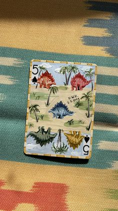 a playing card sitting on top of a colorful cloth covered table with dinosaurs and palm trees