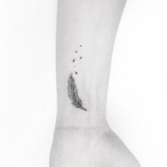 a black and white photo of a feather tattoo on the left ankle, with tiny dots coming out of it