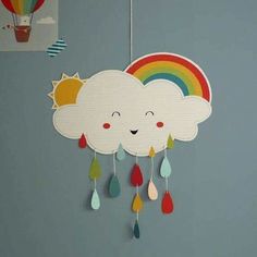 a paper cloud with rainbows and rain drops hanging from it's side on a gray wall