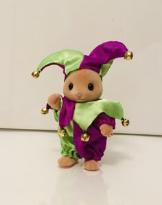 a small stuffed animal wearing a purple and green outfit with bells on it's head