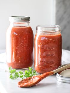 two mason jars filled with red sauce and garnished with parsley next to a spoon