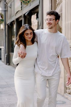 a man and woman are walking down the street holding each other's arm as they smile