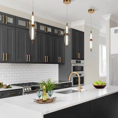 a kitchen with black cabinets and white counter tops, gold accents on the lights above the sink