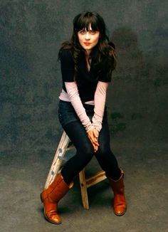 a woman sitting on top of a wooden chair with her legs crossed and wearing brown boots